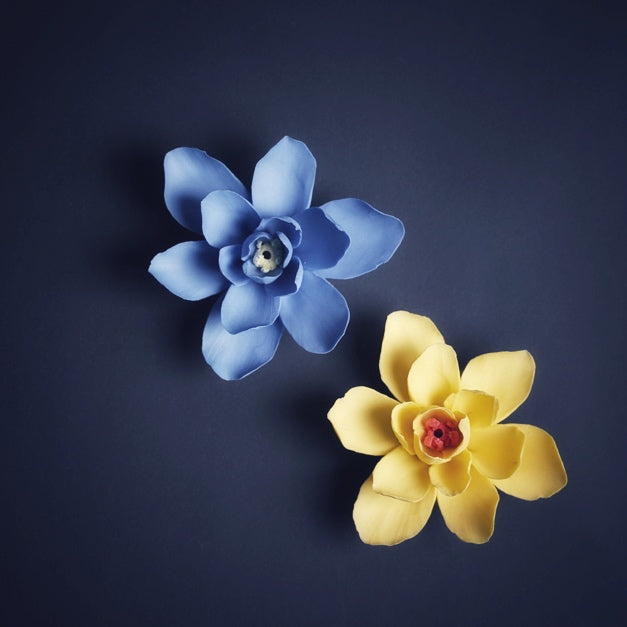 Two ceramic incense holders shaped like flowers, one blue and one yellow, on a dark background.